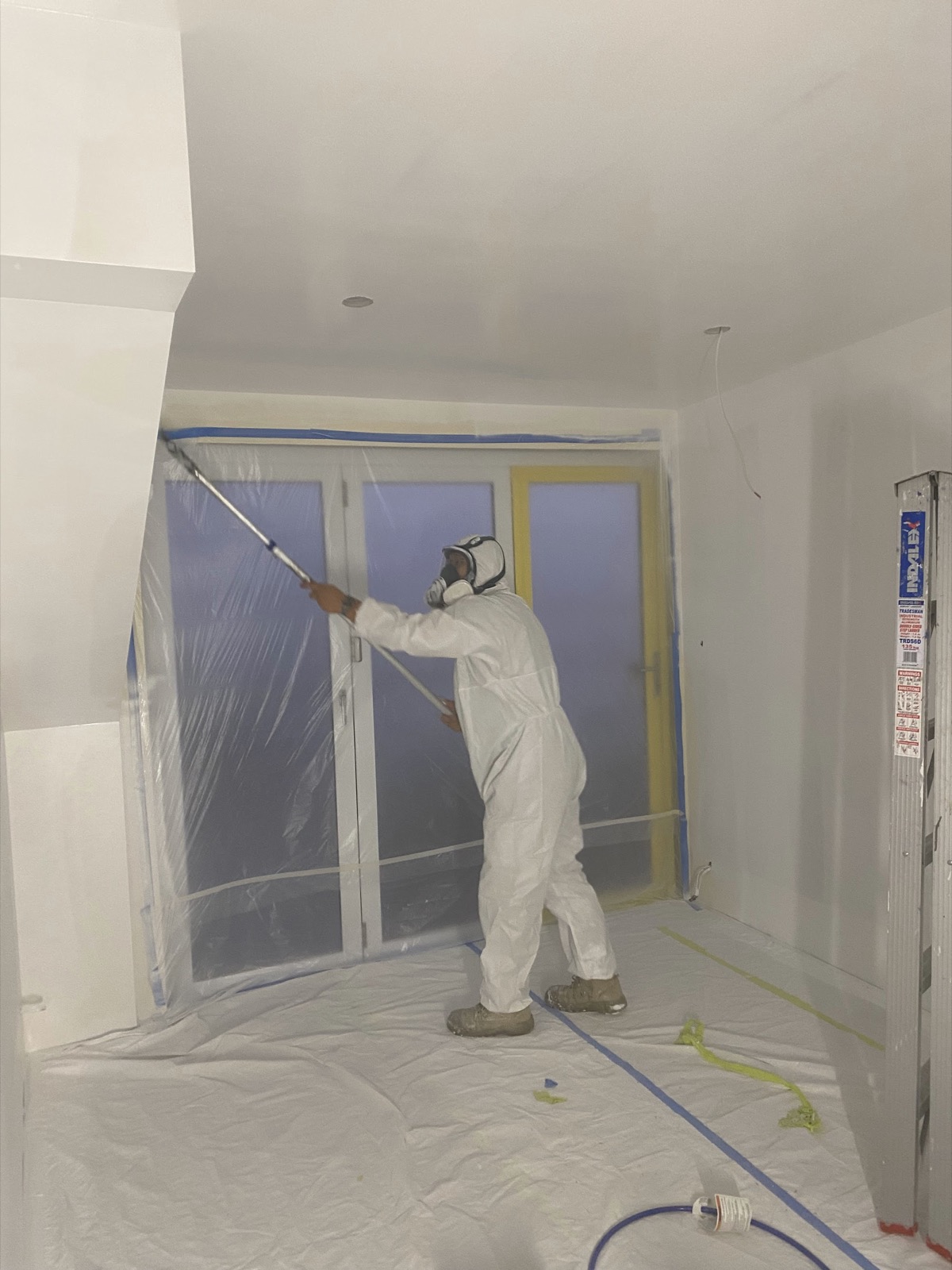 Painter in protective suit spraying a fully masked room